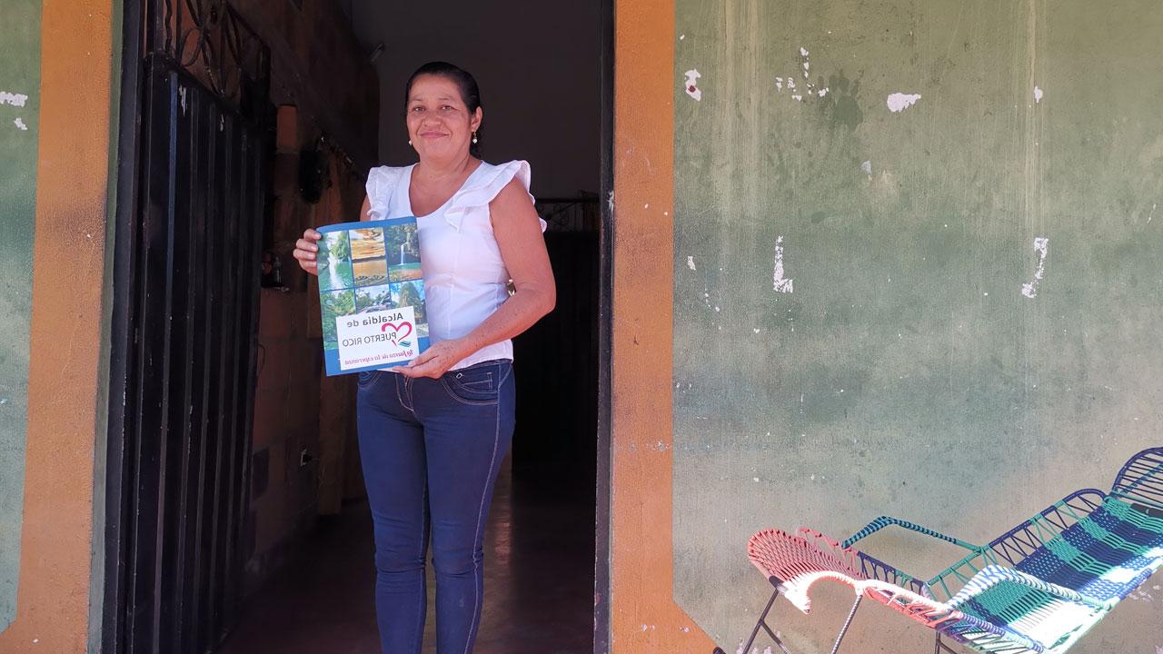 A woman in Colombia stands in a doorway holding her registered land certificate, supported by the Tetra Tech-led land rights program